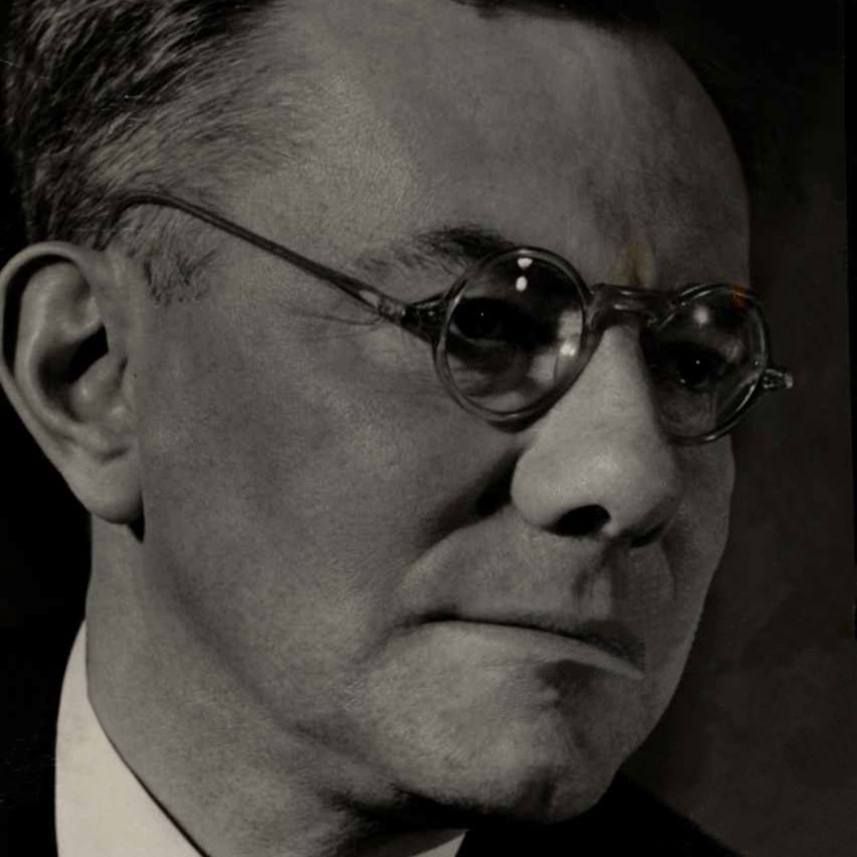 Studioporträt Paul Tillichs im Halbprofil, mit Brille, vor dunklem Grund